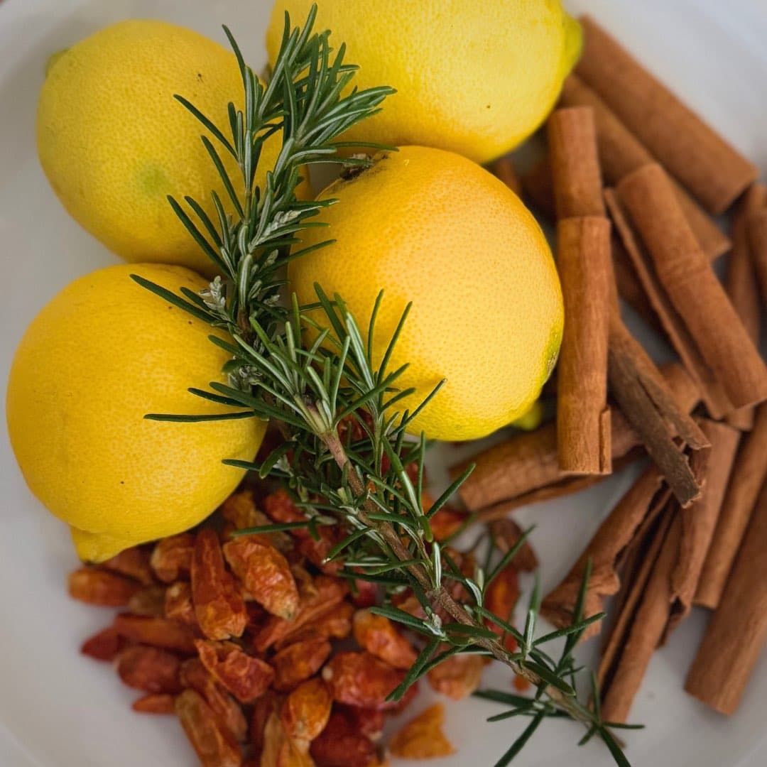 Fresh lemons, rosemary, cinnamon sticks and dried cayenne pods arranged on a plate