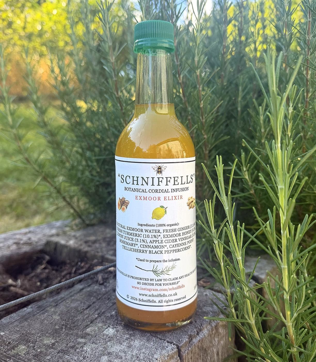A 330ml bottle of Schniffells Exmoor Elixir standing on weathered timber among rosemary bushes